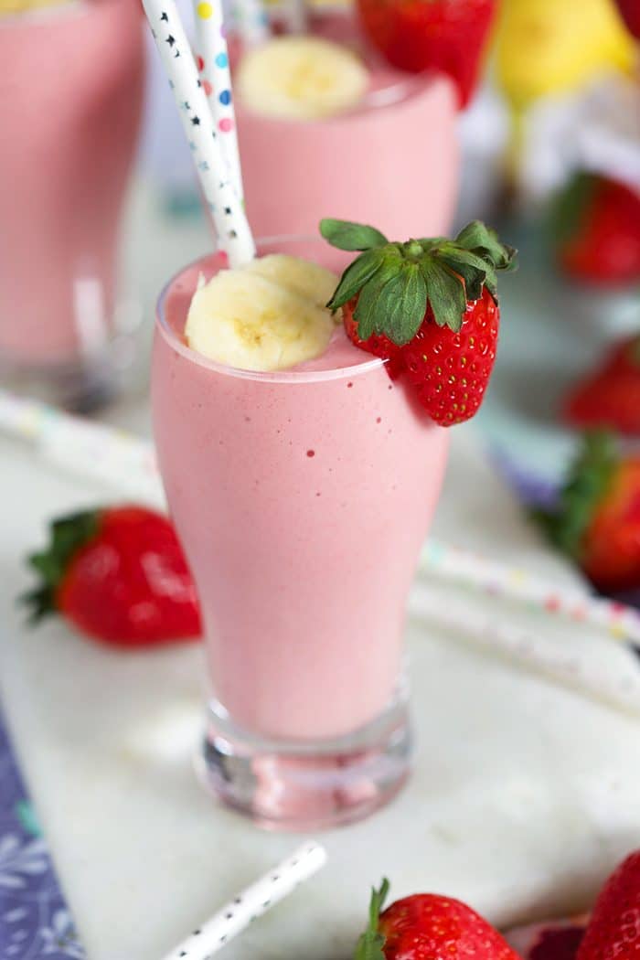 Strawberry Banana Smoothie in a tall glass with a banana slice on top and a fresh strawberry on the side of the glass.