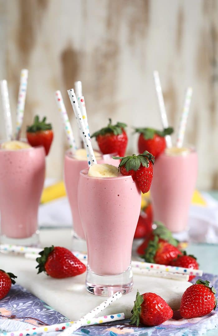 Four Strawberry Banana Smoothies arranged on a marble board with fresh strawberries.