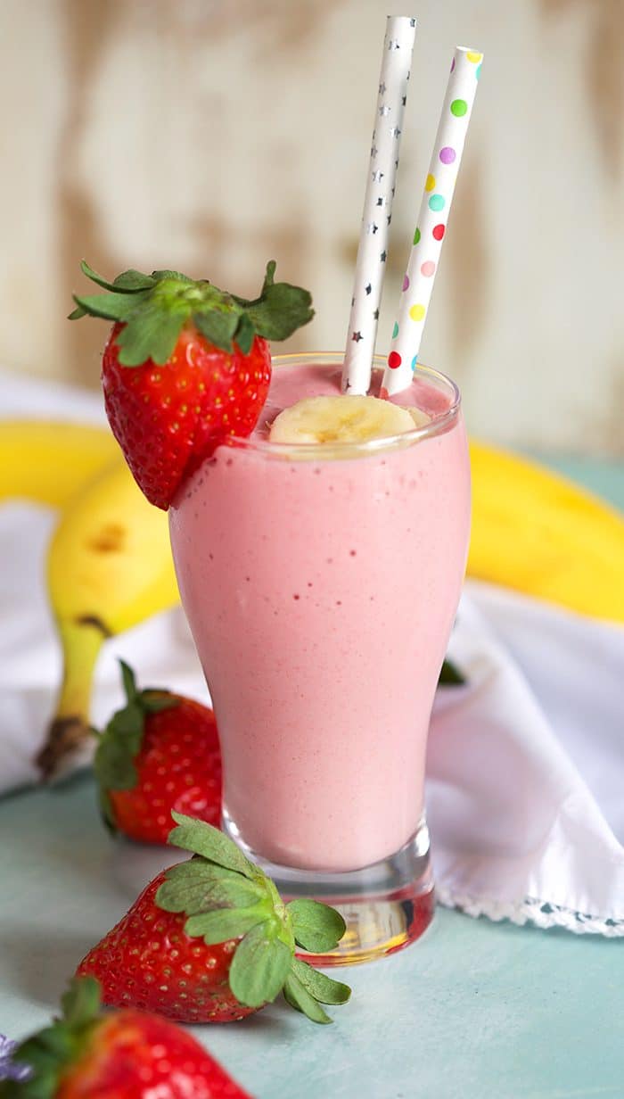 Strawberry Banana Smoothie with two paper straws in a tall glass on a blue background.