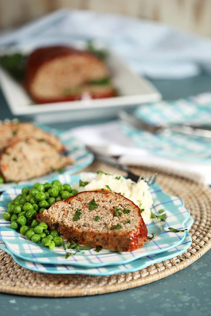Turkey meatloaf on a plaid plate with mashed potatoes and peas.