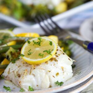 Lemon Baked Cod Loin on a white plate with vegetables.