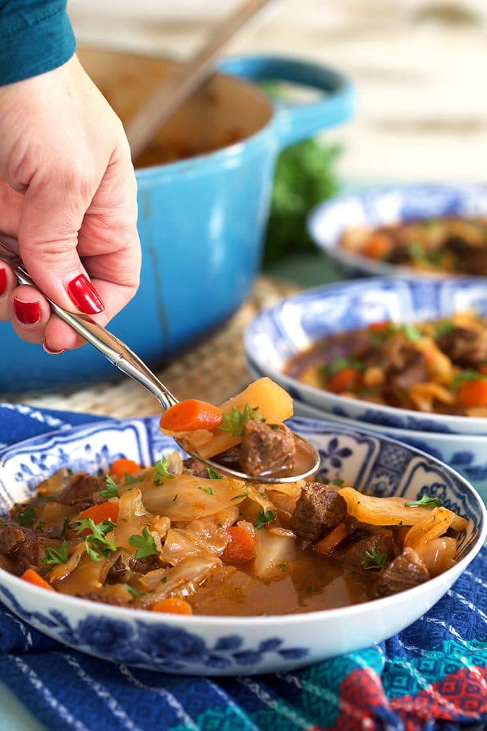 Beef Cabbage Soup recipe in a blue and white bowl with a spoonful above the bowl.