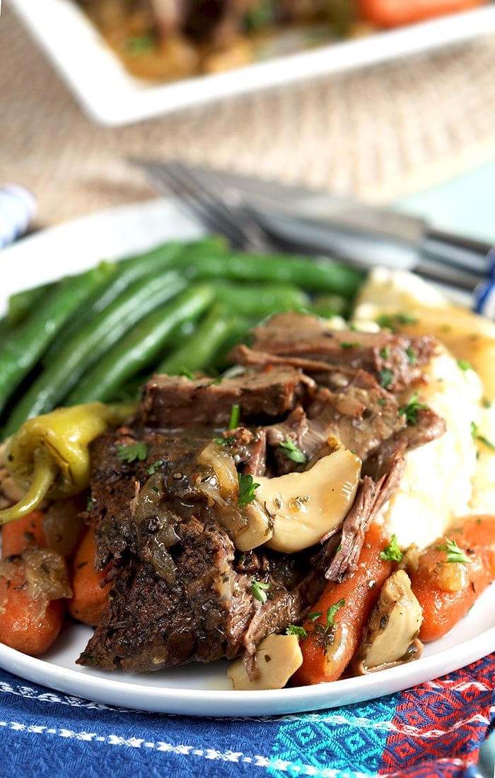 close up of mississippi pot roast on a pile of mashed potatoes with gravy and green beans.