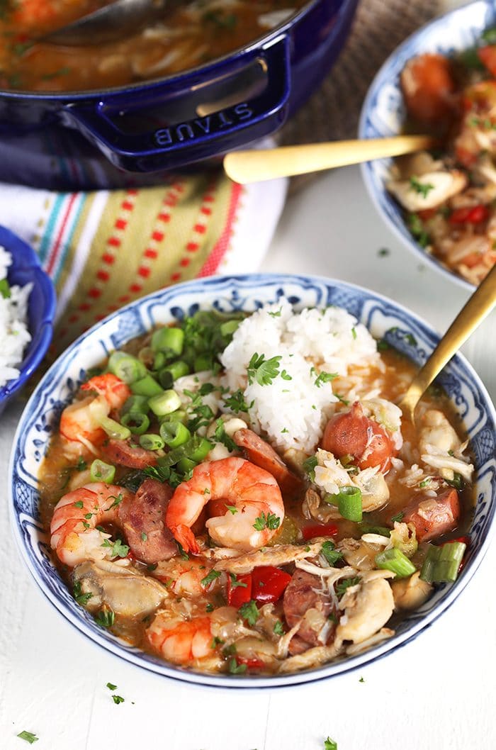 Overhead shot of seafood gumbo with a pile of rice in a blue and white bowl on a white background.