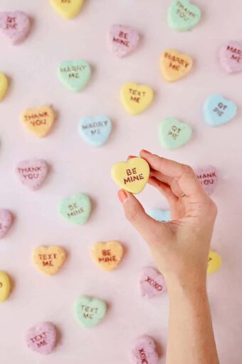 Valentine Conversation Heart Bath Bombs with a hand holding a yellow heart against a pink background.