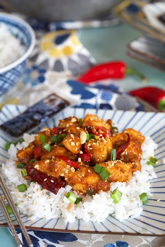 Easy Szechuan Chicken recipe on a bed of white rice on a square blue and white plate with silver chopsticks.