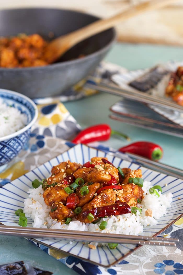 Szechuan Chicken Stir fry on a square plate with white rice and stainless steel chopsticks.