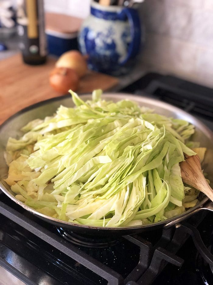 chopped cabbage in a skillet with a wooden spoon on a black gas stove.