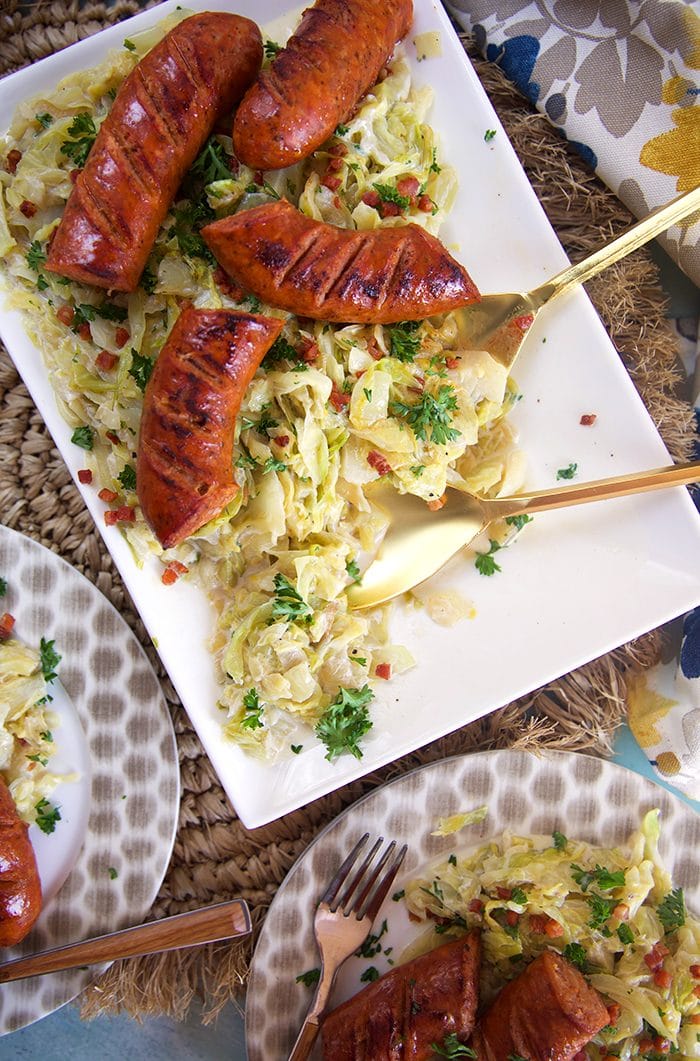 Overhead shot of fried cabbage and kielbasa on a white platter with a gold serving spoon.