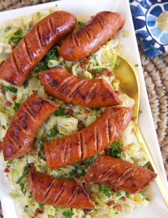 Overhead shot of kielbasa on a bed of fried cabbage on a white rectangular platter.