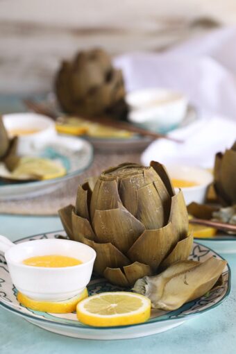 Instant Pot artichokes on a plate with lemon slices and melted butter.