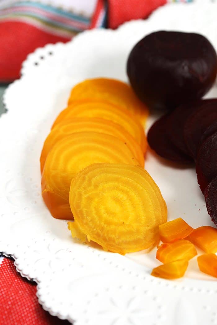 Golden and red cooked beets on a white plate.