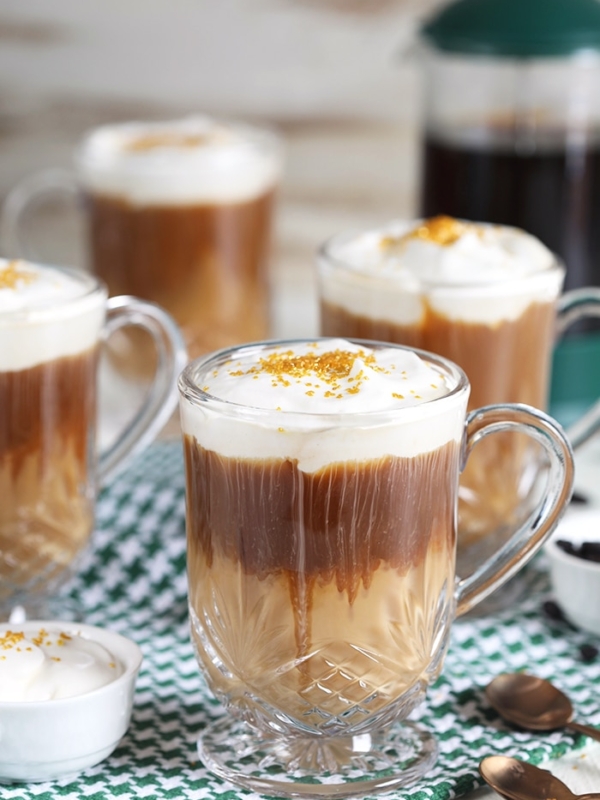 Nutty Irishman in a glass coffee mug with whipped cream and gold sprinkles on a green and white checked napkin.