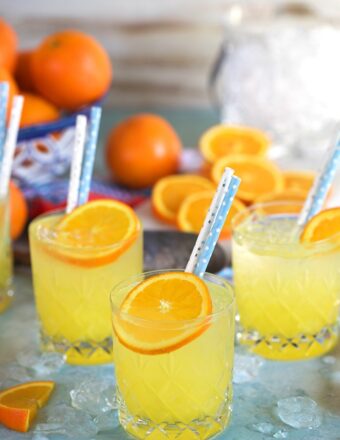Three orange crush cocktails on a blue background with an ice bucket.