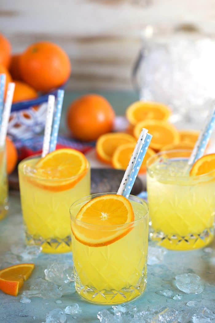 Three orange crush cocktails on a blue background with an ice bucket.
