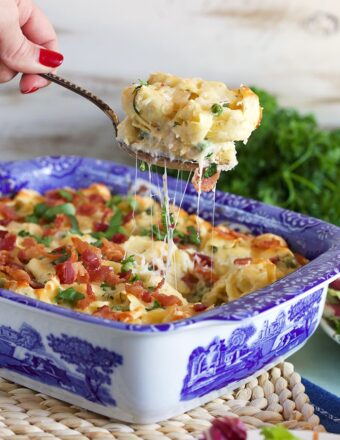 Baked Tortellini al forno in a blue and white casserole with a spoon scooping a serving out and melty stretchy cheese.