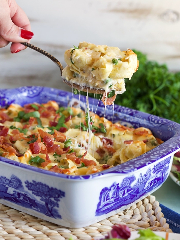 Baked Tortellini al forno in a blue and white casserole with a spoon scooping a serving out and melty stretchy cheese.