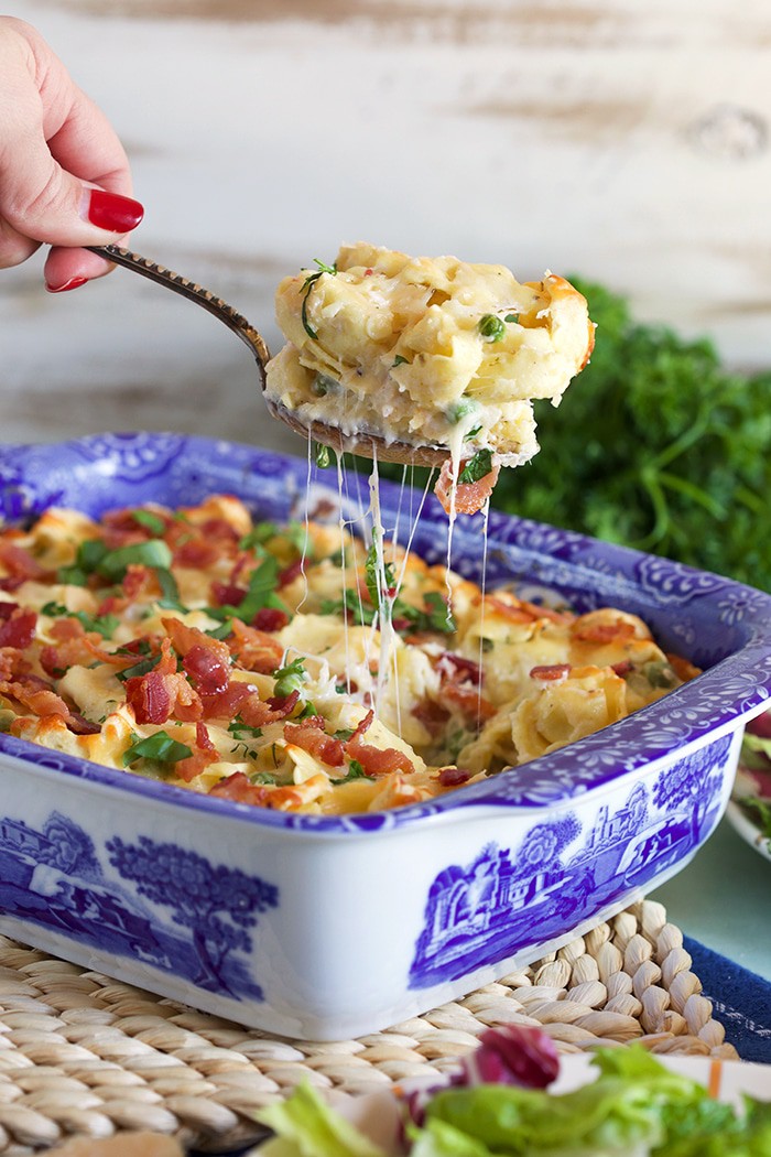 Baked Tortellini al forno in a blue and white casserole with a spoon scooping a serving out and melty stretchy cheese.