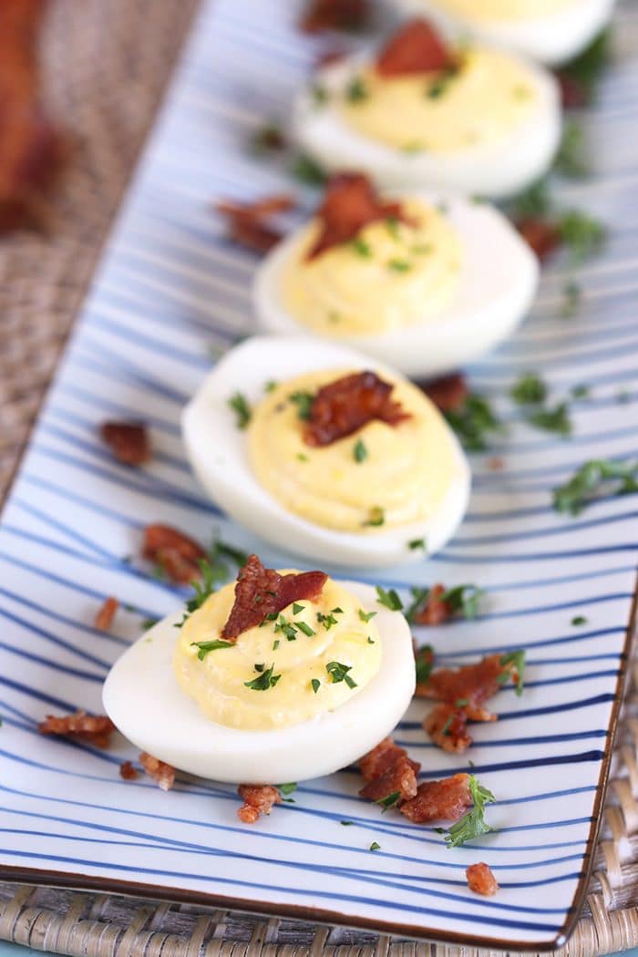 Overhead shot of bacon horseradish deviled eggs on a blue and white striped platter.