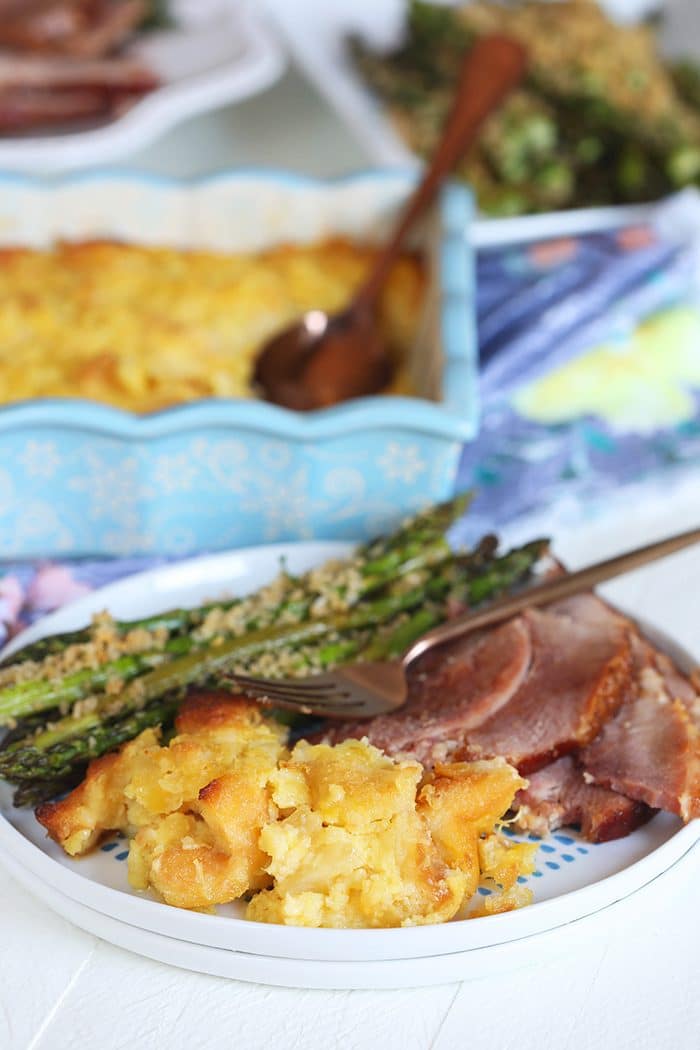 Baked Pineapple Casserole on a white plate with ham and asparagus.