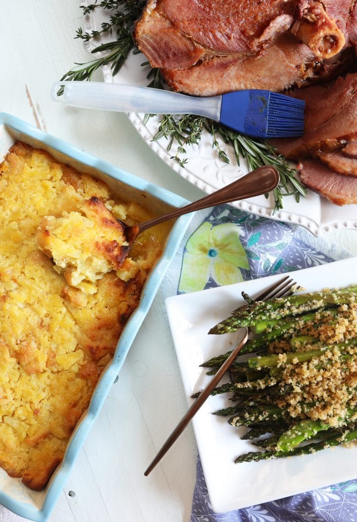 Overhead shot of Baked Pineapple Casserole with a platter of asparagus and a baked ham.