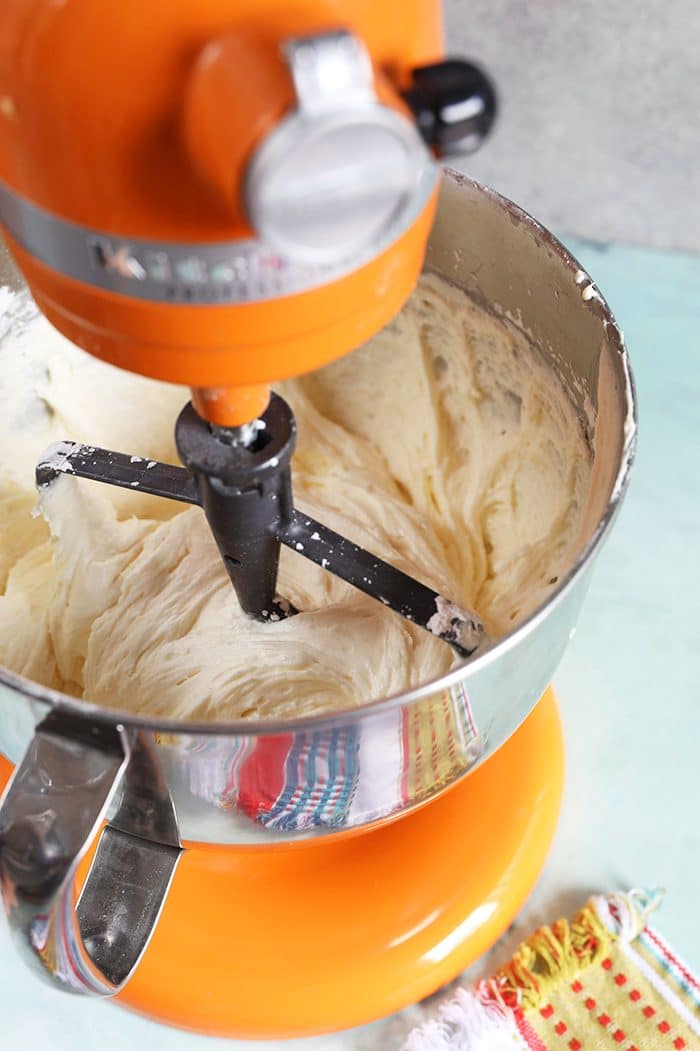 Orange KitchenAid Mixer with Whipped Cream Cheese Frosting in the bowl.