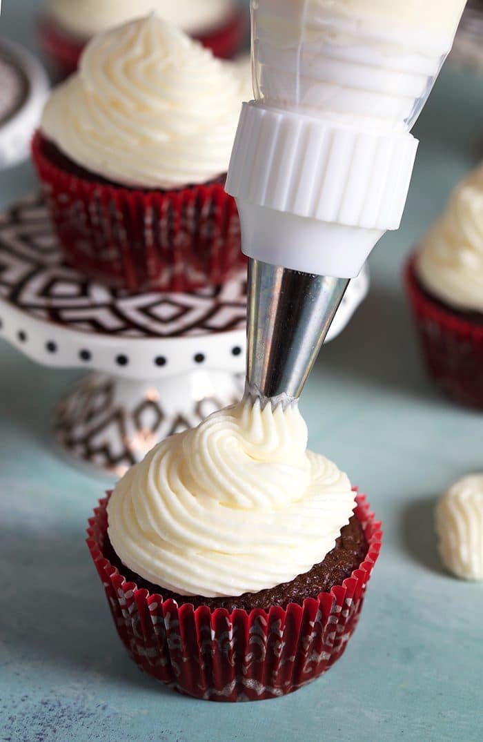 Cream cheese frosting being piped onto a chocolate cupcake.
