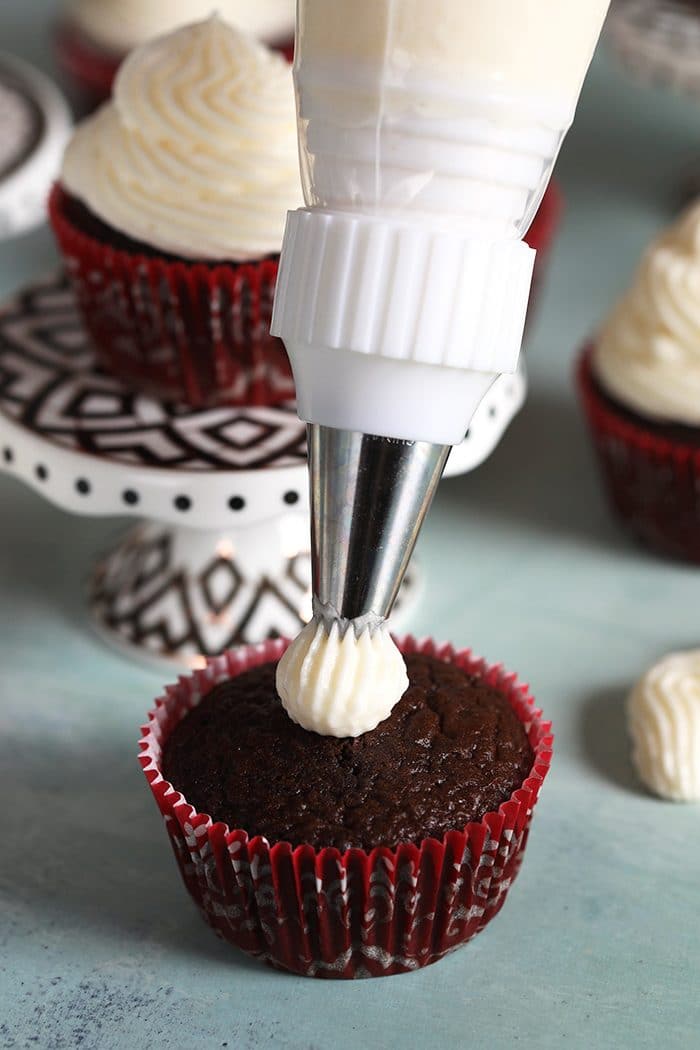 Chocolate cupcake with cream cheese frosting being piped on it.