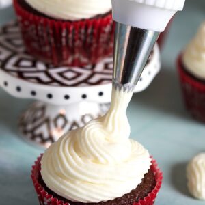 Chocolate cupcake in a red cupcake paper with cream cheese frosting being piped on top.