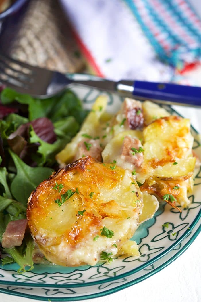 Close up of a serving of ham and scalloped potatoes on a blue and white plate with a salad.