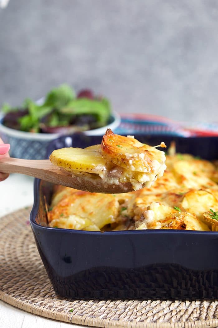 Ham and Scalloped Potatoes in a blue casserole with a wooden spoon scooping out a serving.