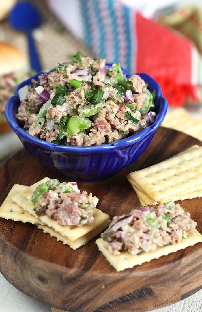 Ham Salad in a blue bowl on a wooden board with crackers.