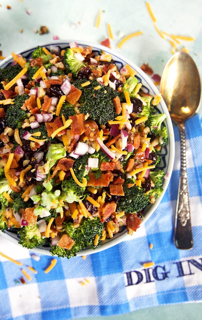 Overhead shot of broccoli salad with bacon on a blue and white checked napkin that says Dig In.