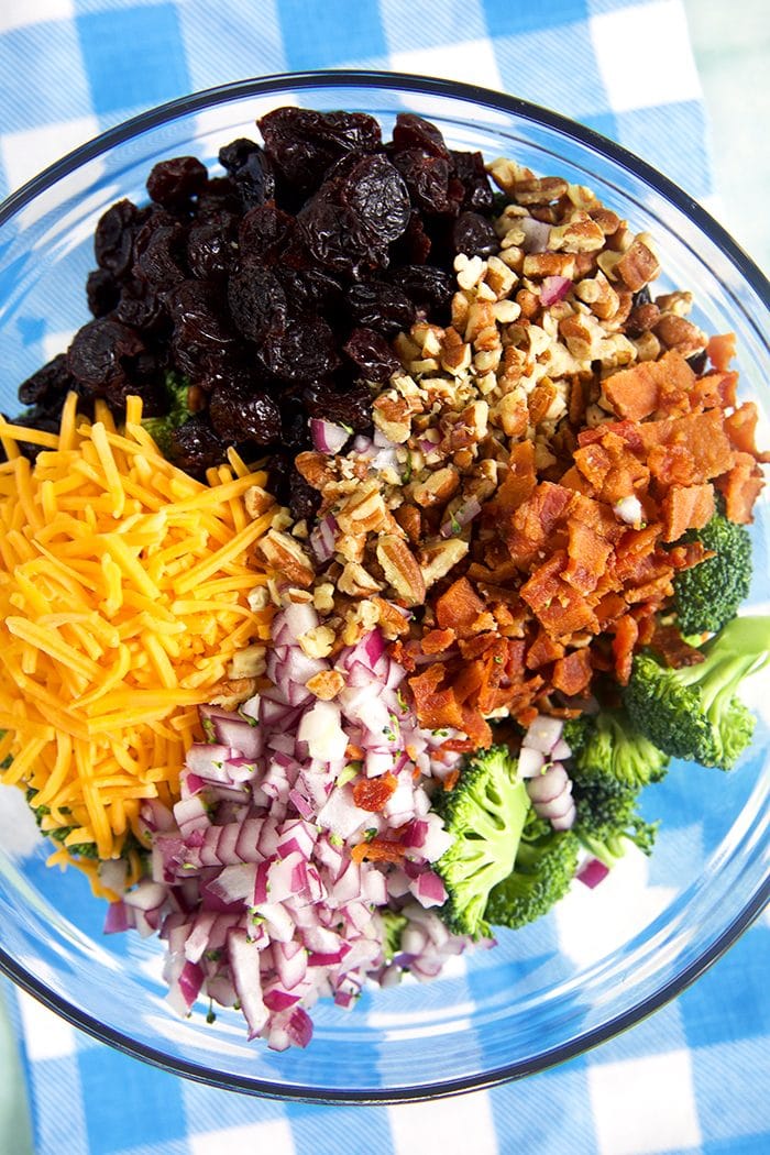 Overhead shot of ingredients for broccoli salad in a glass bowl.