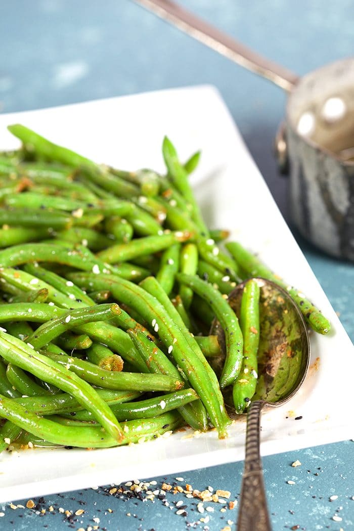 Green beans on a white platter with a silver spoon.