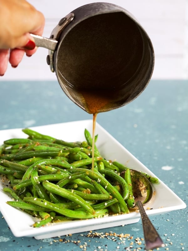 Sauteed green beans on a white platter with brown butter being poured over them.