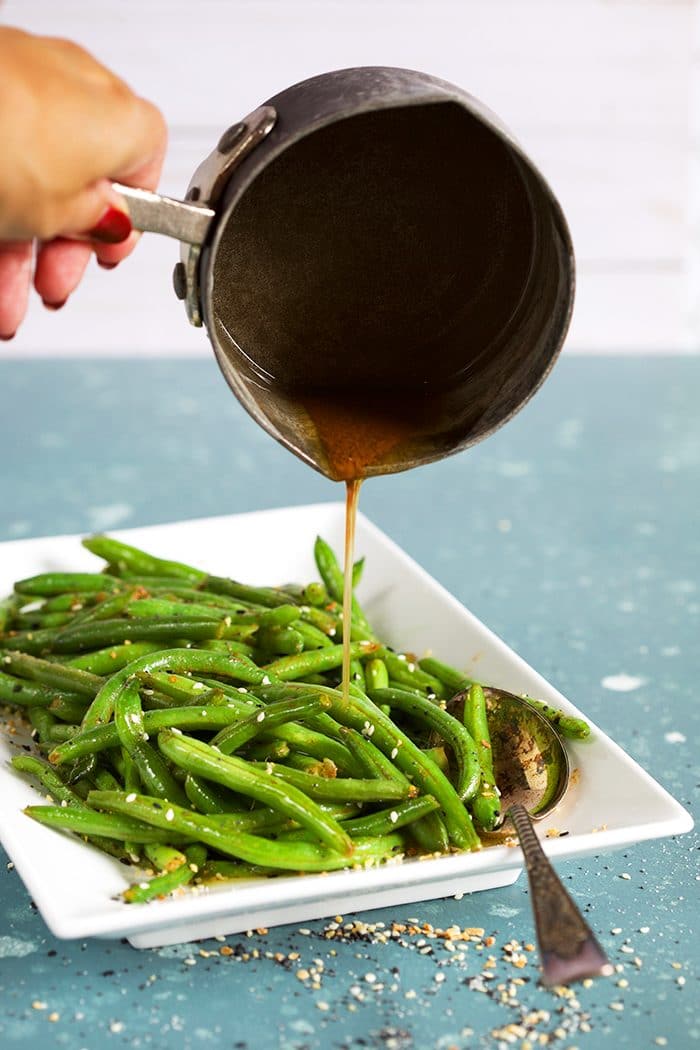 Sauteed green beans on a white platter with brown butter being poured over them.