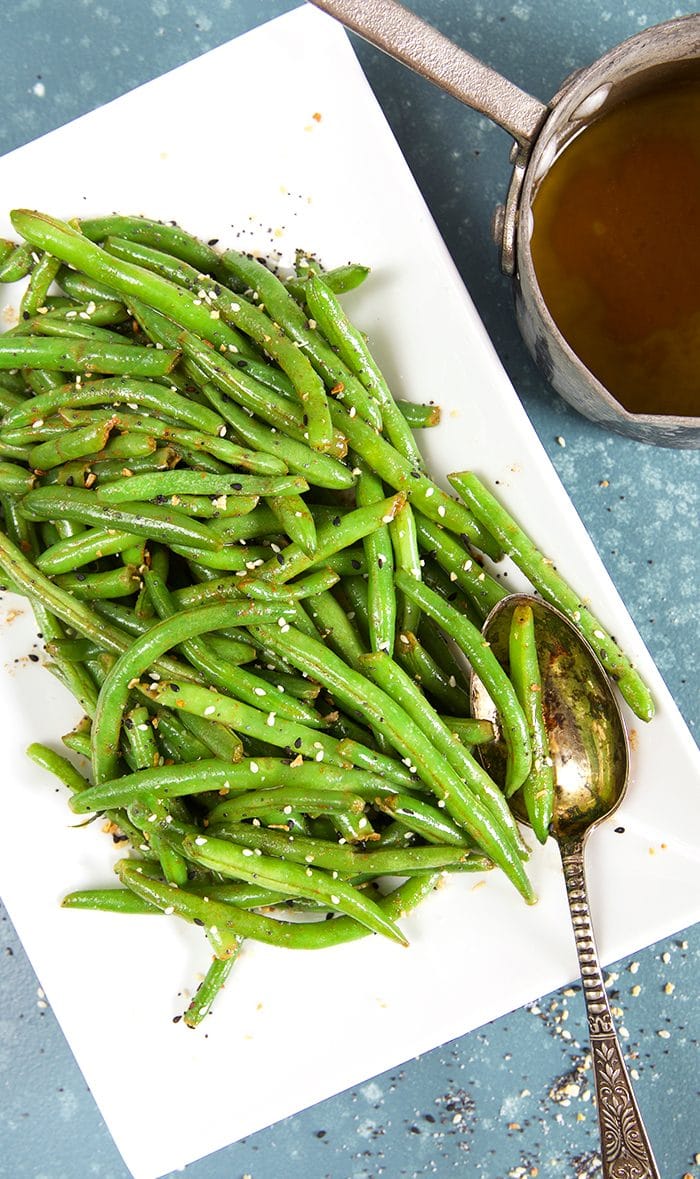 Overhead shot of green beans on a white platter with a silver spoon.