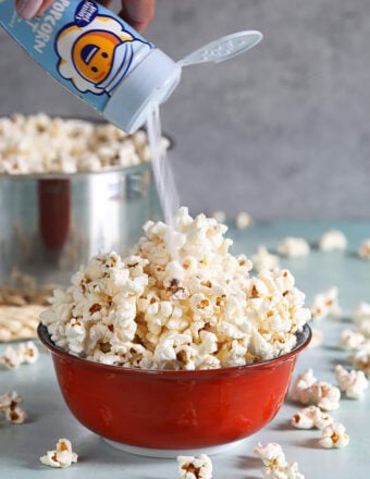 Popcorn in a red bowl with popcorn salt being put on top.