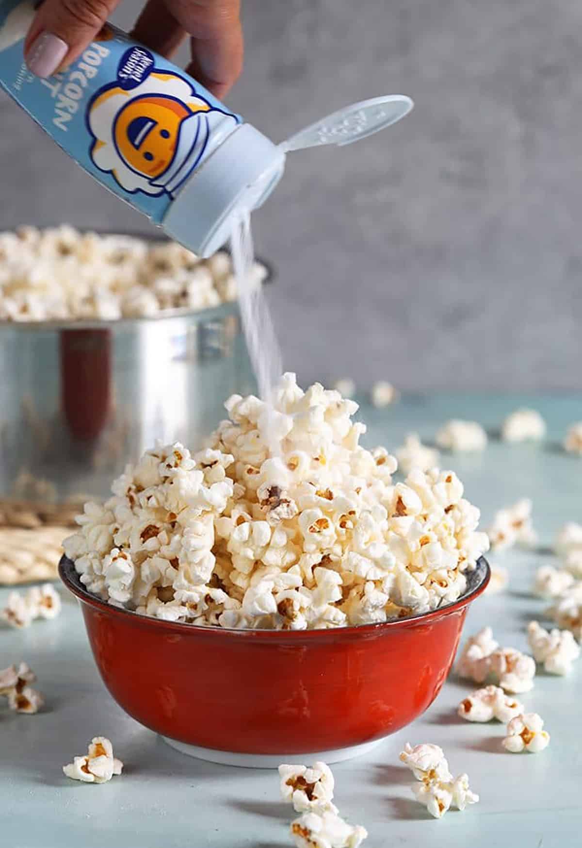 Popcorn in a red bowl with popcorn salt being put on top.