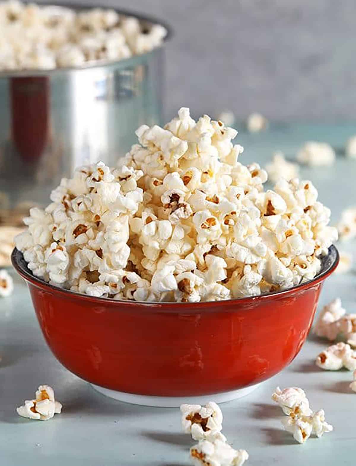 Stovetop popcorn in a red bowl on a blue background.