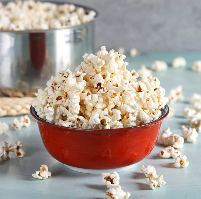 Stovetop popcorn in a red bowl on a blue background.