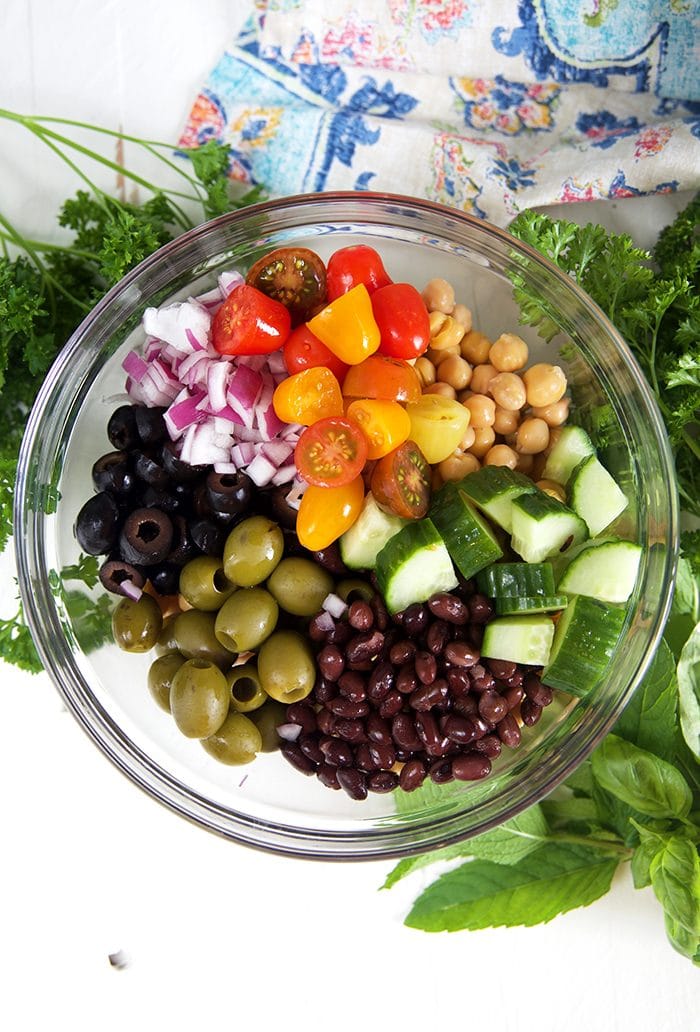 overhead shot of ingredients for chickpea salad in a glass bowl with herbs.