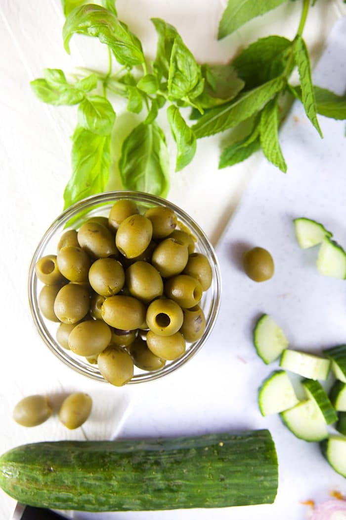 Bowl of green olives with chopped cucumber and herbs.