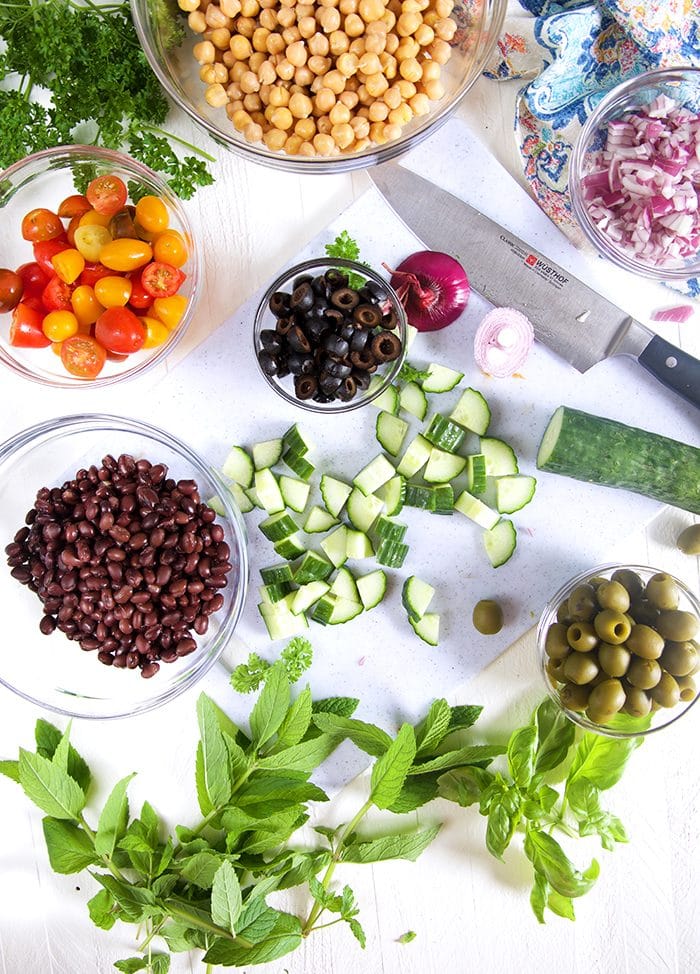 Overhead shot of ingredients for chickpea salad on a white background with a knife.