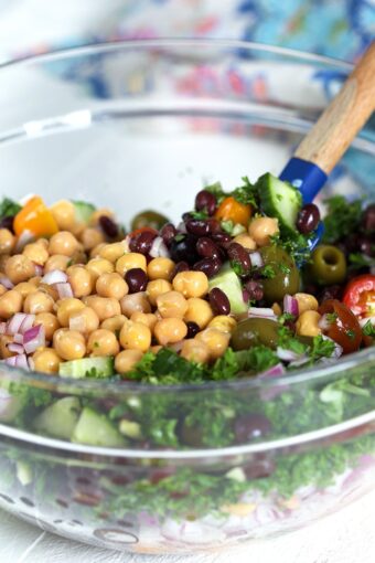 Ingredients for chickpea salad in a glass bowl with a spatula.