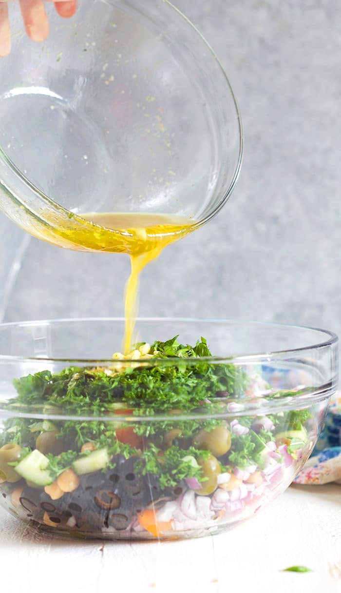 dressing being poured over chickpea salad in a glass bowl.