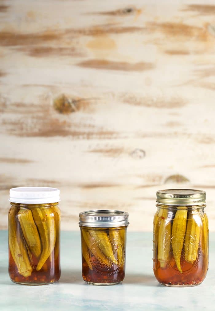 Three jars of pickled okra on a blue background.