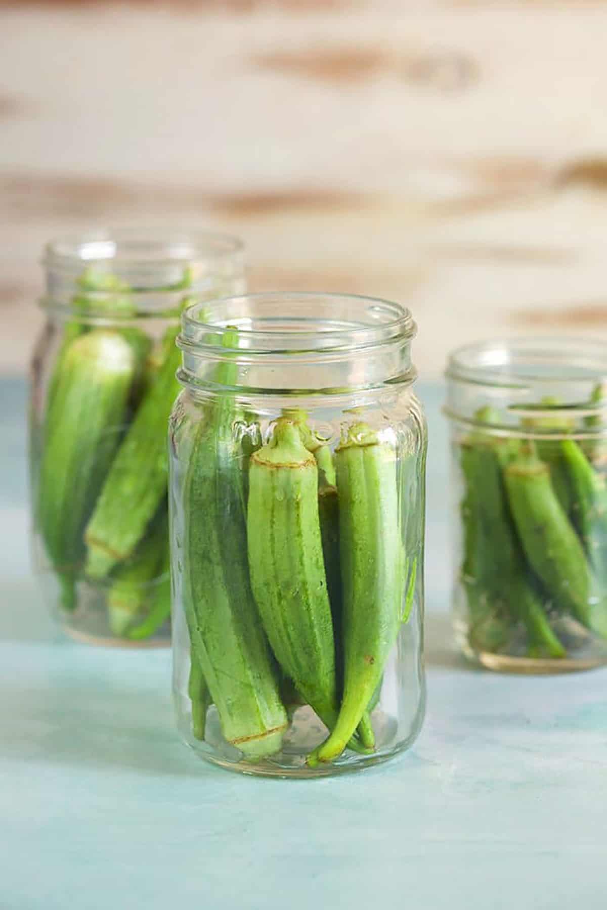 Okra in canning jars on a blue background.