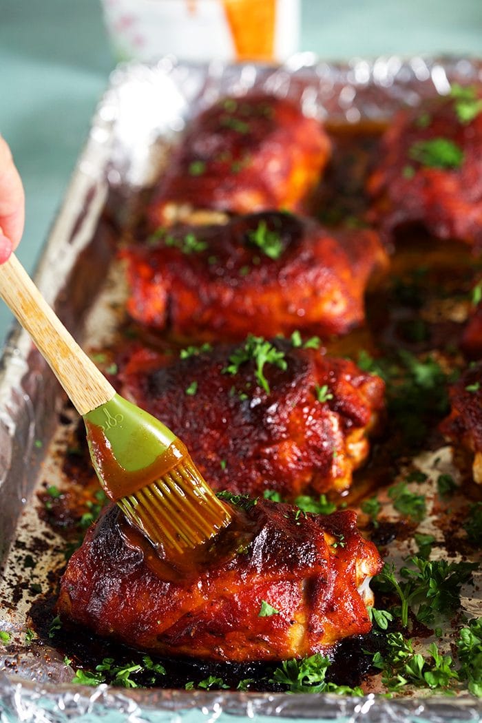 BBQ Chicken on a baking sheet with barbecue sauce being brushed on a thigh.
